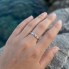 Silver infinity ring with separate round stones beside the infinity symbols, worn on a woman's hand beside water