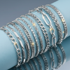 Stainless steel chain bracelets displayed on a light blue cylindrical stand with blue grey background and mirror reflection