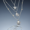Stainless steel ocean charm layered necklace set on blue grey gloss background with mirror reflection