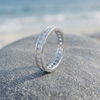 Single silver-tone stone-set ring angled on a coastal rock