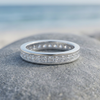 Single silver-tone stone-set ring resting on a grey beach rock